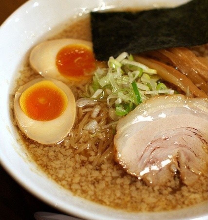 Bowl of ramen with sliced eggs, pork, seaweed, and green onions in broth.